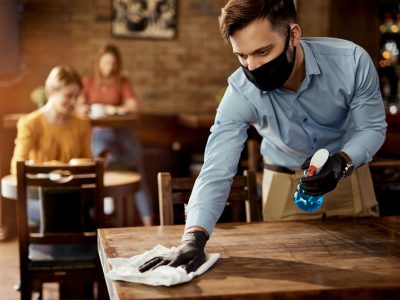 homem de mascara higienizando uma mesa num restaurante