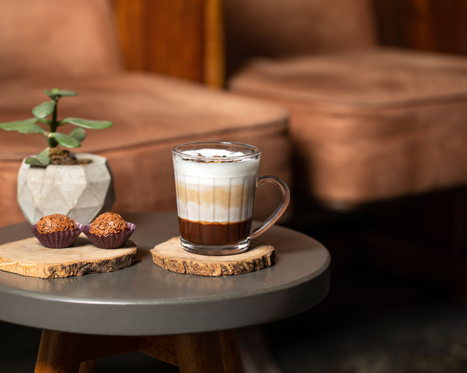 Xicará de café com leite numa mesa com doces ao lado, do Sofá Café