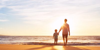 pai e filho de mãos dadas olhando o mar