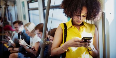 Mulher negra, de camisa amarela , usa seu ceular de pé, em um metrô