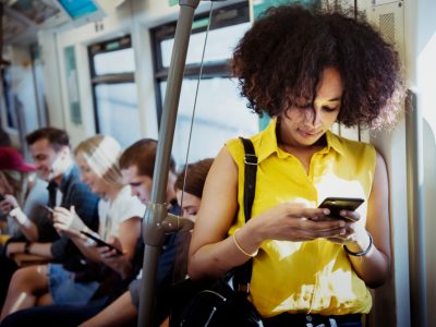 Mulher negra, de camisa amarela , usa seu ceular de pé, em um metrô