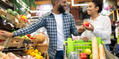 Casal fazendo compras no mercado com um carrinho cheio de frutas e legumes