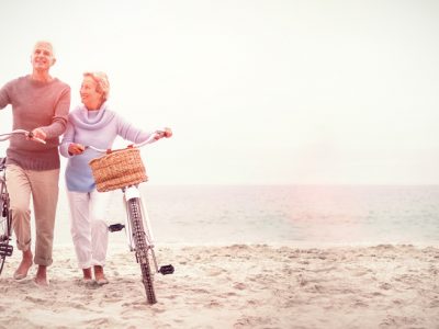 Casal de idosos, passeando ao lado de suas bicicletas na praia