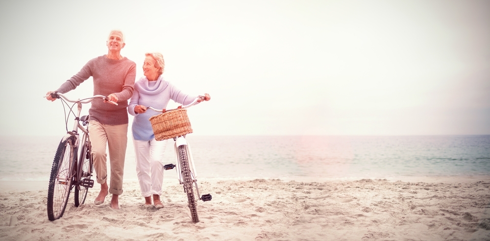Casal de idosos, passeando ao lado de suas bicicletas na praia
