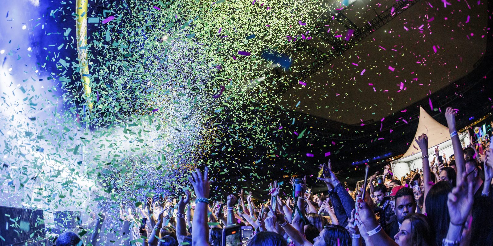 Foto do show na festa da Alelo, com o público vibrando e papéis coloridos caindo
