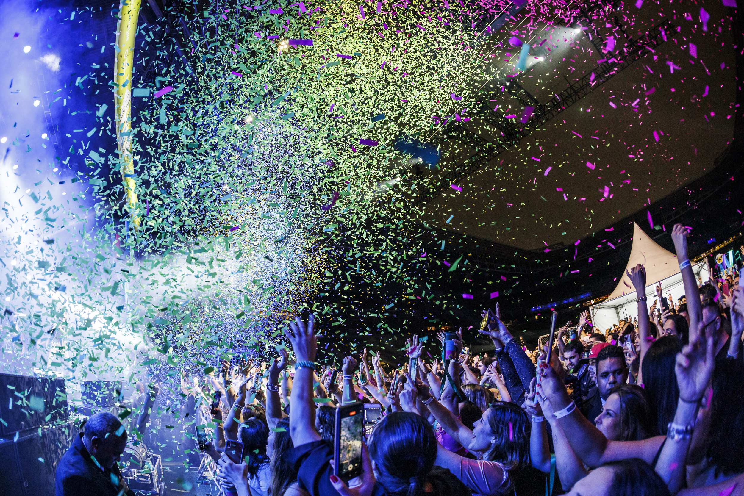 Foto do show na festa da Alelo, com o público vibrando e papéis coloridos caindo