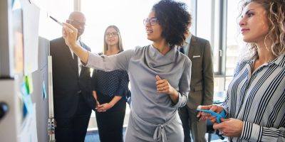 Mulher escrevendo em um quadro branco durante uma reunião de equipe