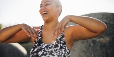 Mulher careca, negra, de top de ginástica, sorrindo